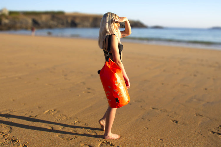 girl on beach looking out to sea wearing the orange strawberry dry bag by salty kit 