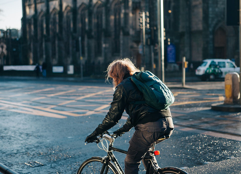 a girl cycling through a city in the rain with a waterproof backpack on her back