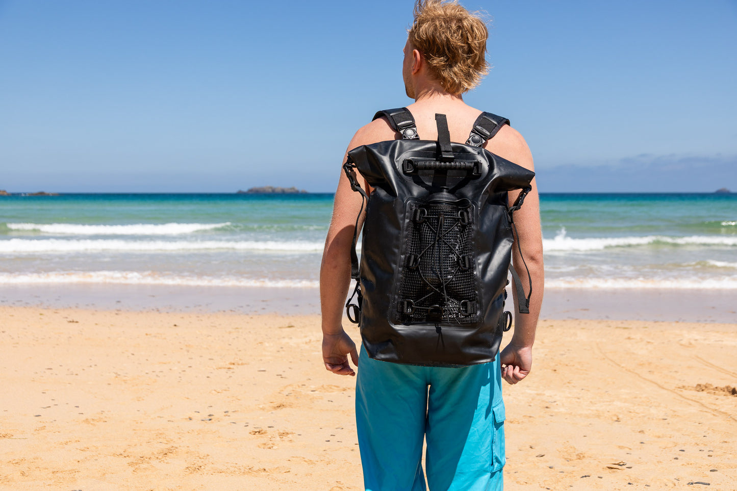 the smart black 30 litre salty kit backpack with detachable comfort straps styled by man on a Cornish beach