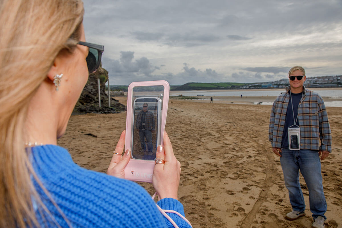 a girl taking a photo of her friend with the pink salty kit waterproof phone case on the beach