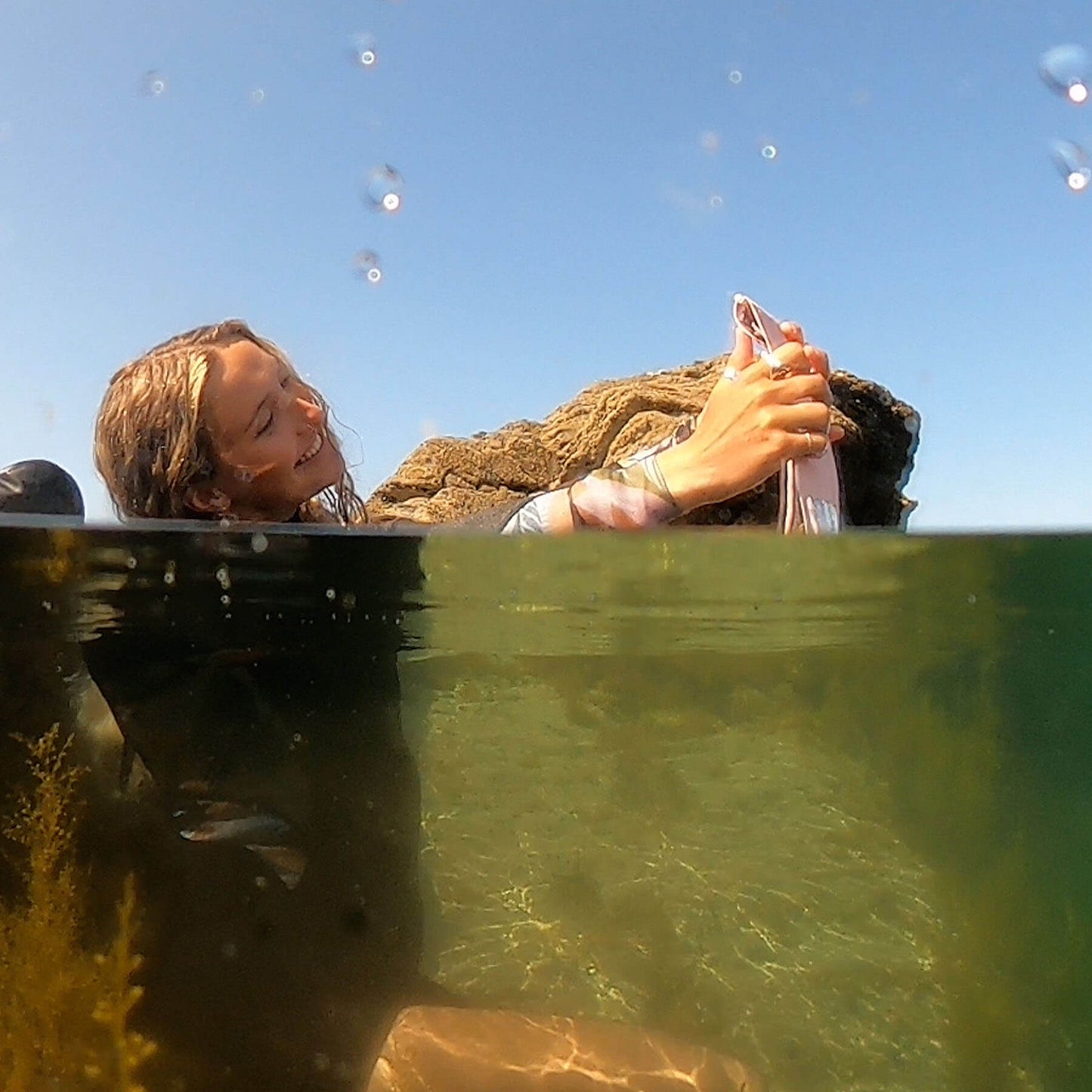 a girl taking a selfie in a pool using a pink phone pouch by salty kit