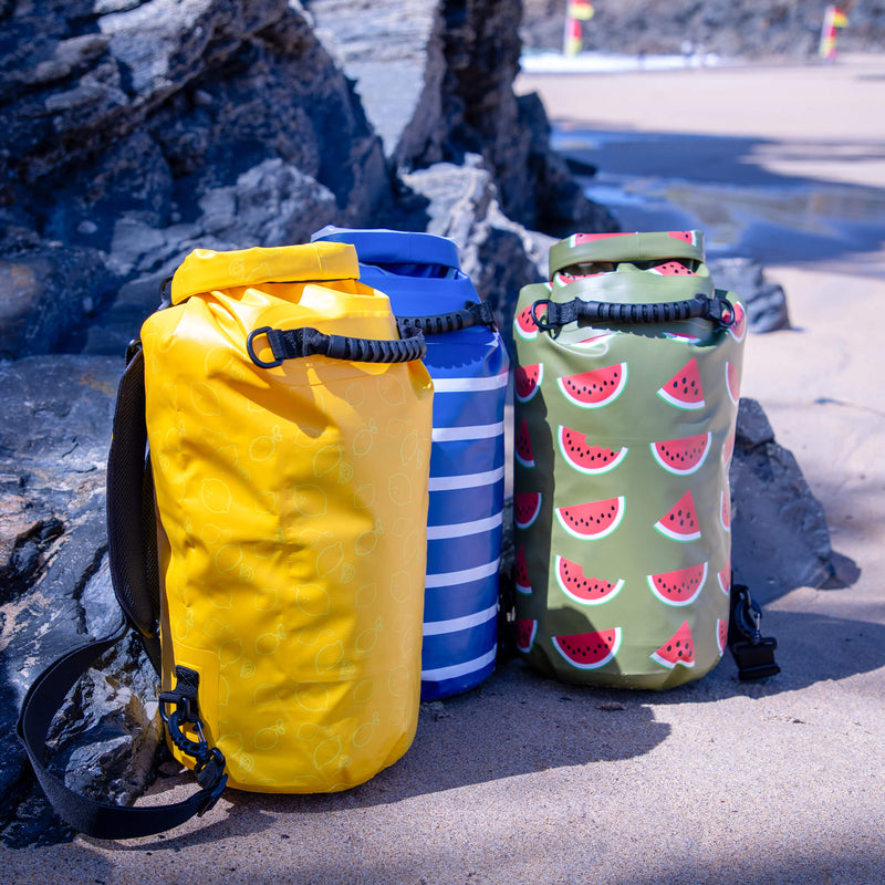 Three colorful waterproof bags on a rocky beach.