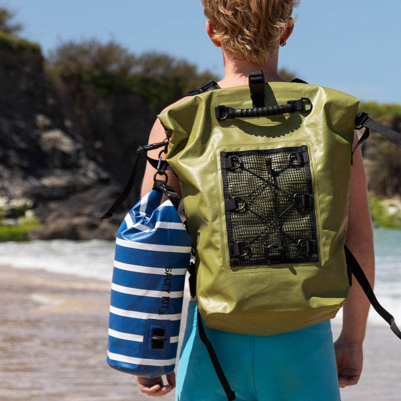 Two people walking on a wooden path by a beach, carrying bags.