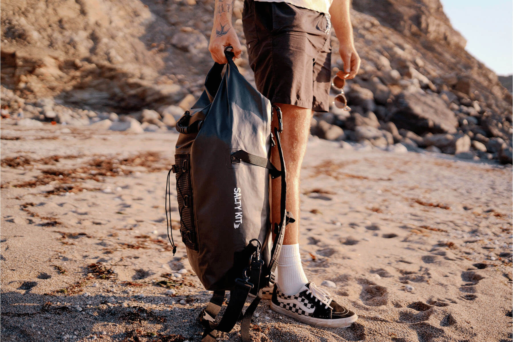 the salty kit 30 litre backpack is the ultimate bag build for adventure and comes in olive and black colours. this shows a man holding the waterproof bag on the beach
