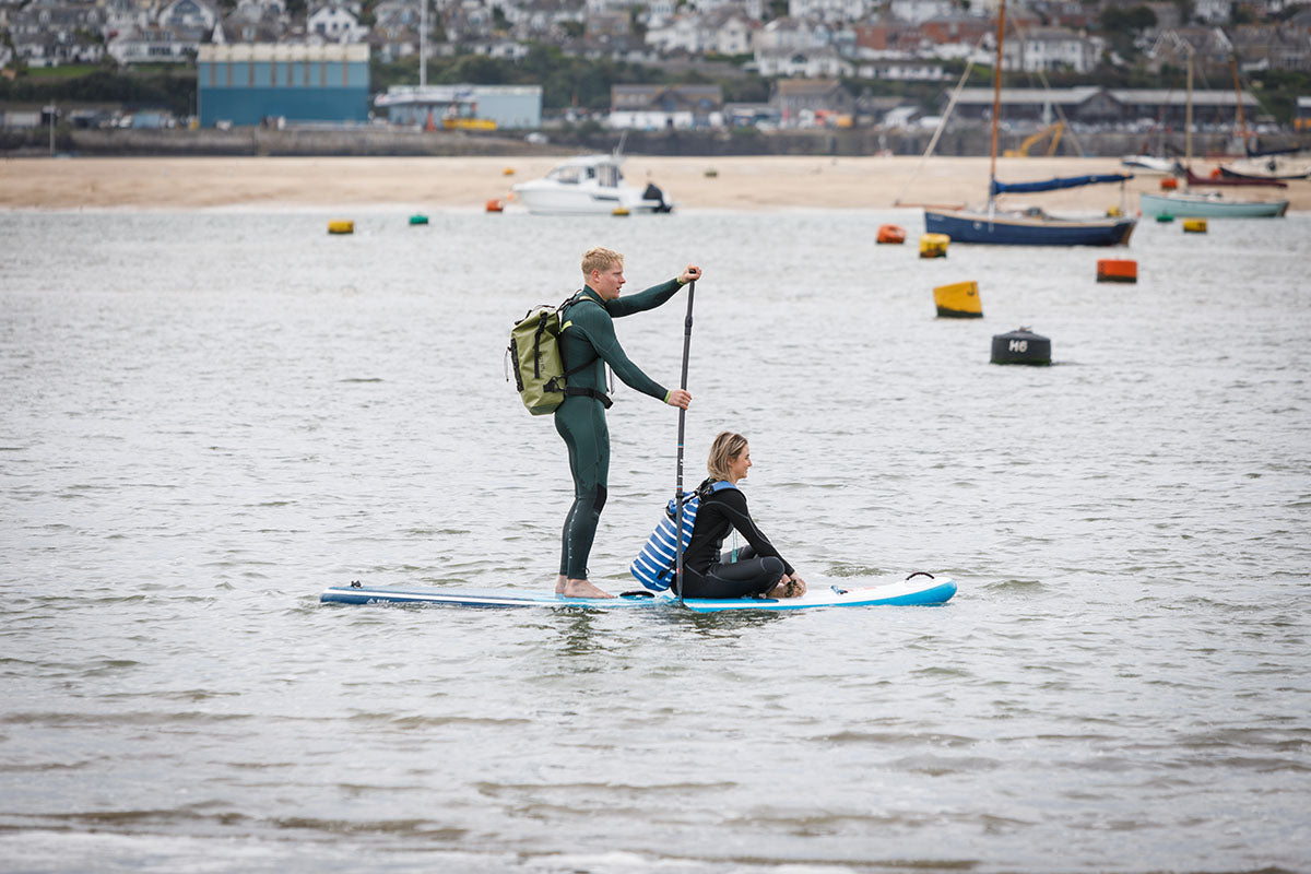 a couple paddleboarding on the camel estuary wearing salty kit backpacks