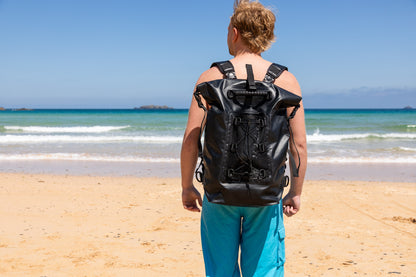 the smart black 30 litre salty kit backpack with detachable comfort straps styled by man on a Cornish beach 