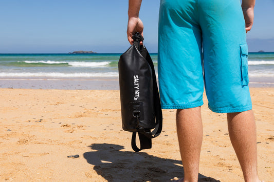 man holding small black dry bag by salty kit standing on sunny harlyn beach in cornwall